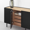 A modern sideboard cabinet with matte black doors and a light natural wood top and drawer fronts, shown with one door open to reveal storage. A black wire vase with dried stems sits on the tabletop against a clean white wall.