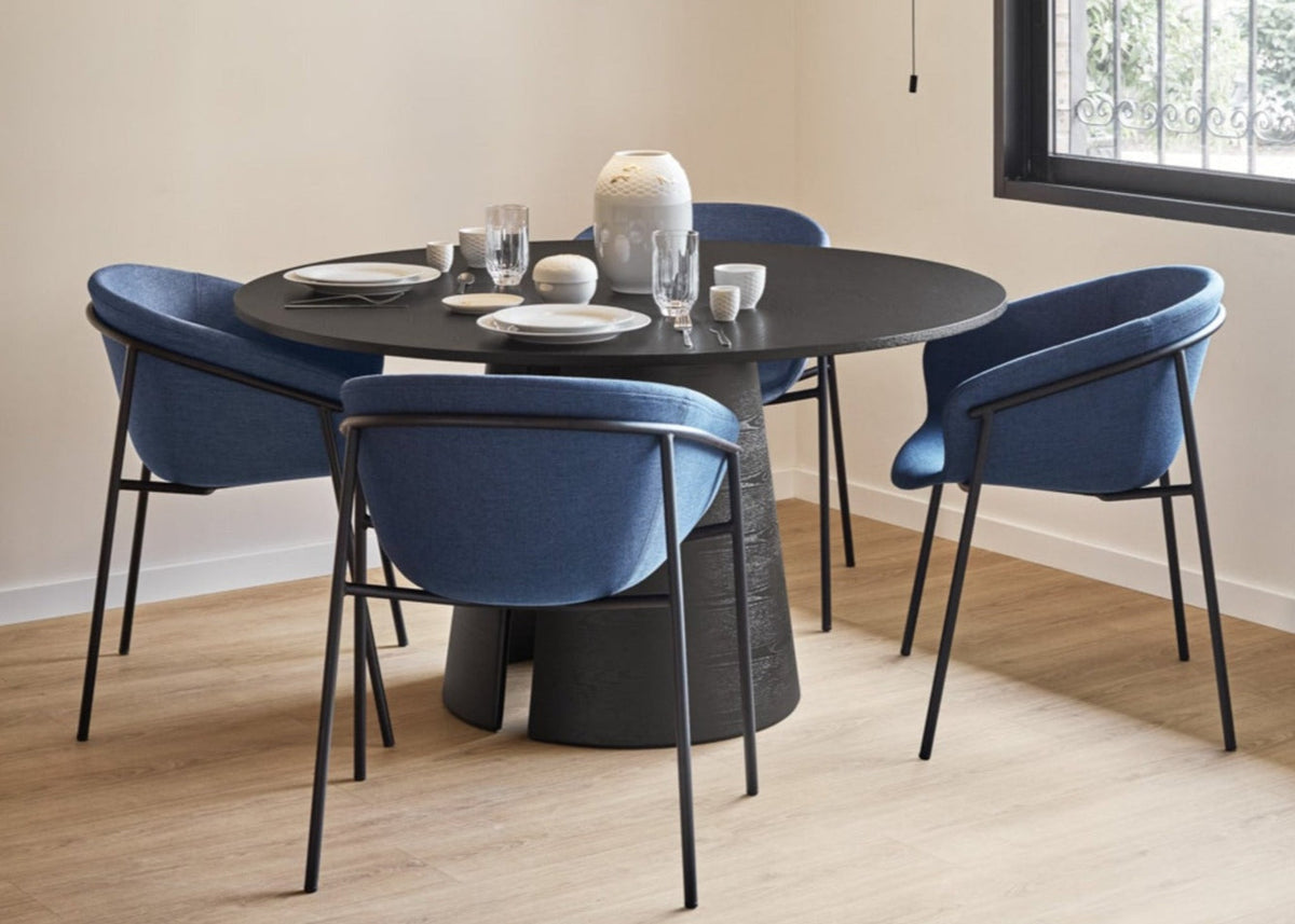 Dining room with a round black table and blue chairs, featuring a modern chandelier.