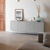 A modern ribbed gray sideboard or console cabinet in a minimalist living room setting, styled with a framed print, small vases, and a blue glass vase with dried grass.