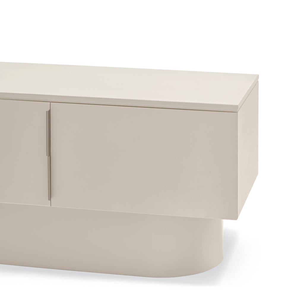 A close-up of a modern low-profile sideboard or media console in a warm off-white or light beige finish, showing the top surface, cabinet doors, and a rounded cylindrical base against a plain white background.