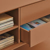 Close-up of a terracotta-colored wooden cabinet with one drawer pulled open, revealing records inside, alongside open shelving with stacked records.