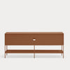 A modern low-profile sideboard or console table with a warm terracotta brown finish, featuring a single drawer with a circular cutout handle and an open lower shelf supported by slim legs, set against a solid light gray background.