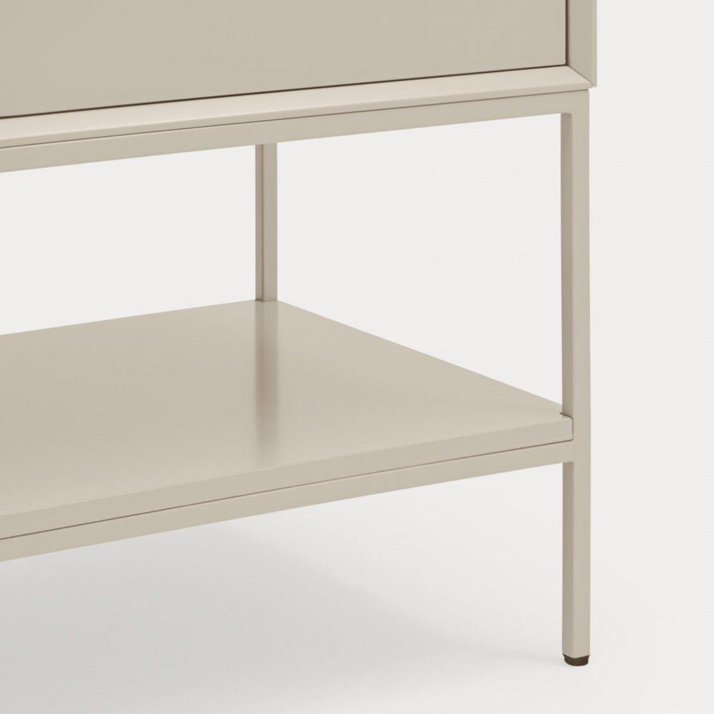 Close-up of a light beige or warm off-white furniture piece showing a drawer front, open shelf, and slim metal legs against a plain light background.