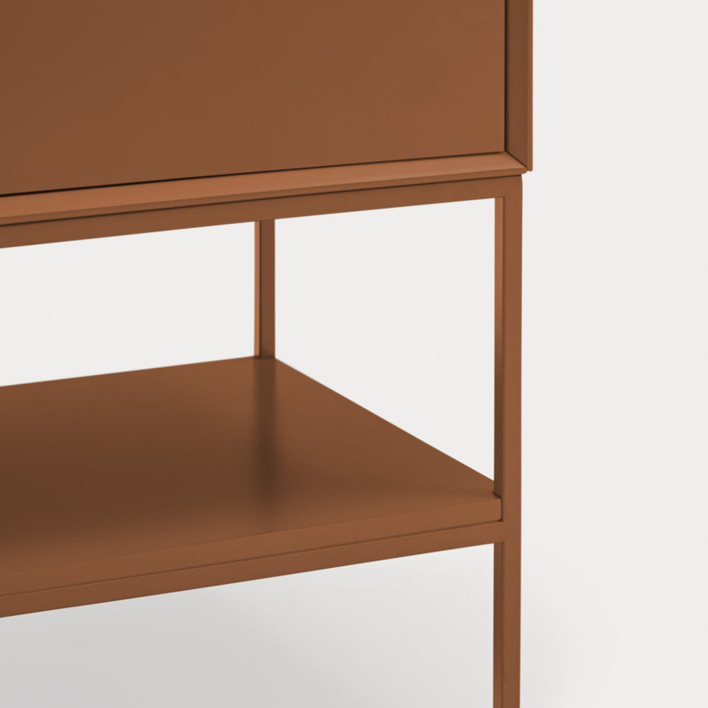 Close-up of a modern cabinet or side table with a warm brown finish, showing the front of a drawer, open shelf, and slim legs against a light gray background.